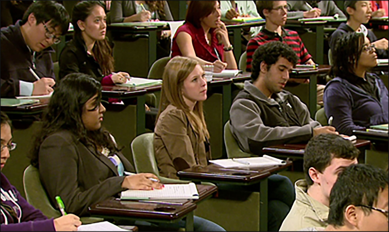 A group of people sitting in an auditorium taking notes.