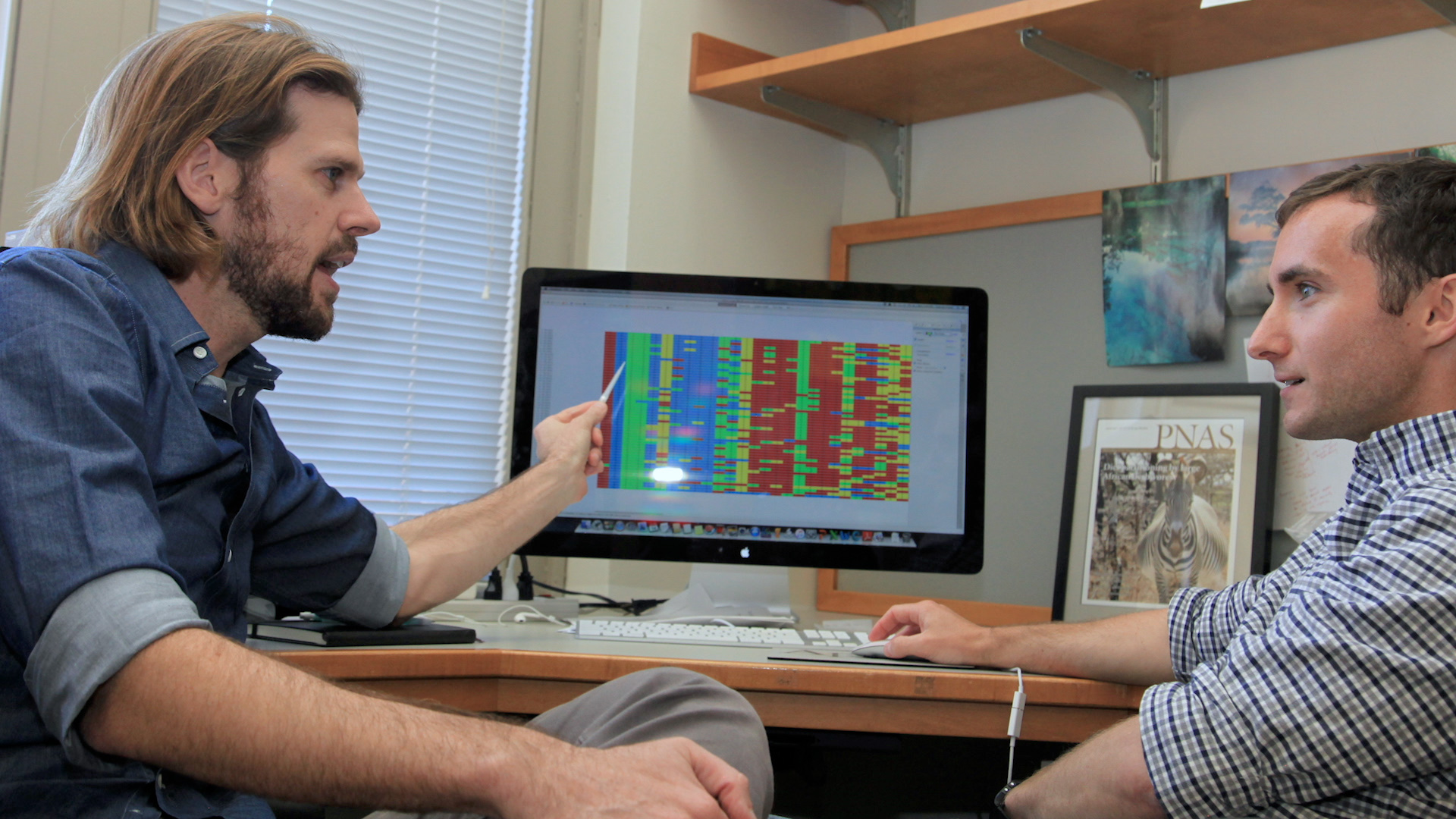 Two researchers are seated at a desk discussing DNA metabarcoding data that appears on a computer screen.