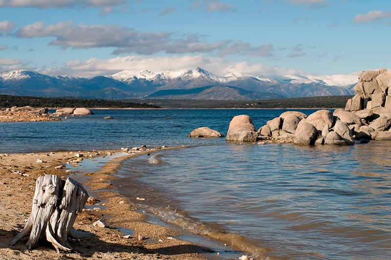 A rocky shoreline with mountains and clouds in the distance.