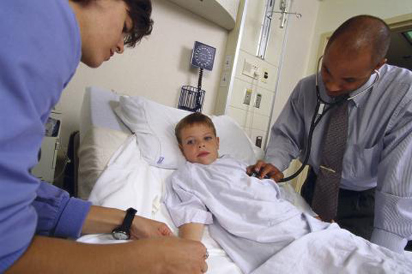 A boy in a hospital bed receiving treatment from medical professionals.