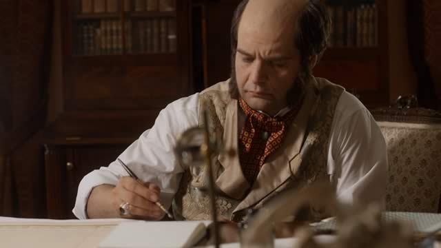 An actor portraying Charles Darwin writes at his desk